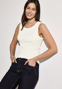 Canotta bianca senza maniche con scollatura rotonda abbinata a jeans di denim scuro con cuciture visibili e tasche laterali.