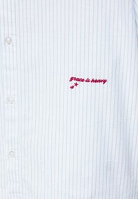 White and light blue striped button-up shirt with red embroidered text "grace is heavy" and a small star and cherry detail.