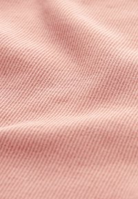 Tissu côtelé rose doux avec des plis subtils et de fines lignes verticales créant une texture délicate et des ombres légères sur la surface.