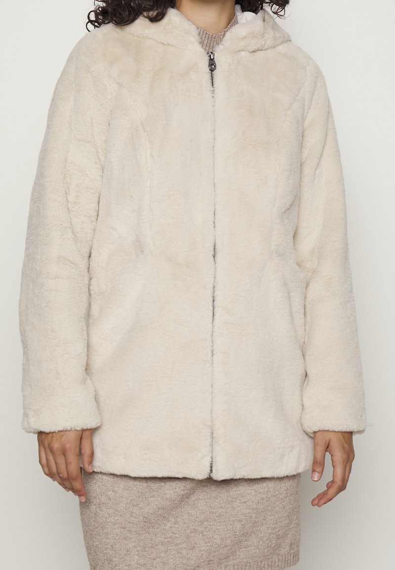 Veste à capuche en fausse fourrure couleur crème avec une fermeture éclair à l'avant, des poches latérales et une texture douce. Présente une coupe décontractée et des manches longues.