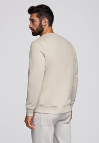 Felpa beige con collo girocollo, maniche lunghe, polsini a coste e una texture liscia, abbinata a pantaloni di colore chiaro.