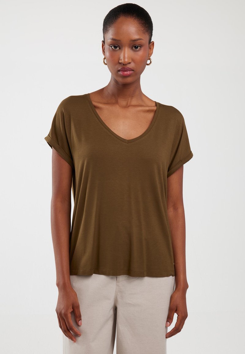 Oliwkowy t-shirt w serek z krótkimi, zawiniętymi rękawami, wykonany z miękkiej tkaniny. Luźny krój z lekko zaokrąglonym dołem.