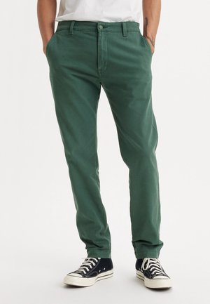 Chinos en coton verts avec une coupe droite, dotés d'une fermeture à bouton, de poches latérales, associés à des baskets montantes noires.