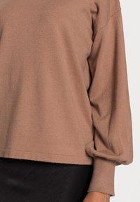 Brązowy sweter dzianinowy o luźnym kroju, z opuszczonymi ramionami i długimi rękawami. Teksturowana tkanina o miękkim, gładkim wykończeniu.