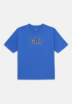 Camiseta de algodón azul con cuello redondo y mangas cortas, que presenta un logo bordado en blanco de "GAP" en la parte delantera. Textura suave, corte regular.