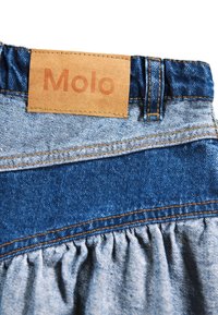Denim skjørt med en samlet nedre kant. Har en lærlabel med "Molo" på livbåndet. Blåtoner og gule sting er synlige.