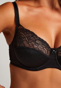 Svart spetsbehå med underwire, prickig textur, blommig spetsdetaljering och en liten satinrosett i mitten. Justerbara band ingår.