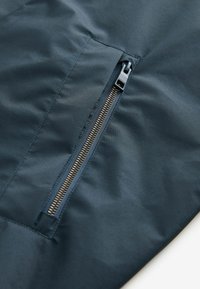 Tâmplă albastră marină cu o textură netedă prezintă o borsetă laterală cu fermoar și detalii de cusătură vizibile. Fermoarul este de culoare argintie cu un dispozitiv de prindere din plastic.