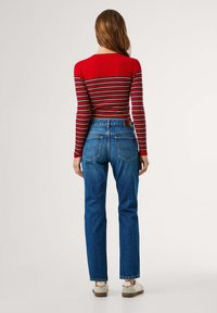 Top de manga larga rojo con paneles acanalados y franjas horizontales multicolores, combinado con unos jeans de denim azul de cintura alta con bolsillos traseros.