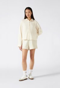Lichtgekleurde blouse met kraag en knopen, van een textuurstof, gecombineerd met bijpassende shorts. Model draagt witte sokken en sneakers.