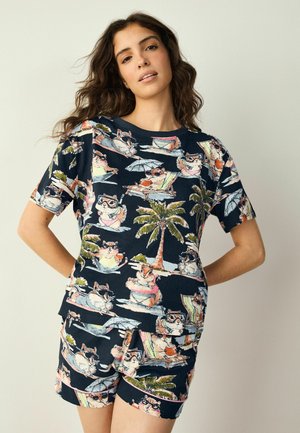 Ung kvinde iført matchende marineblå shorts og t-shirt med et legende print af dovne hamster og palmer.