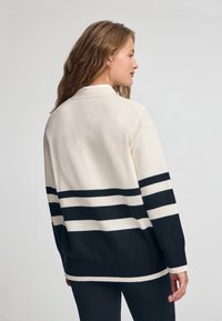 Strick-Cardigan in Creme mit marineblauen Streifen. Verfügt über einen Kragen-Ausschnitt, gerippte Säume und Bündchen sowie eine lässige Passform.