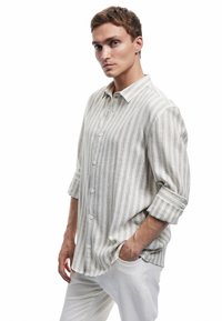 Camisa de botones ligera a rayas en color beige con sutiles líneas grises. Cuenta con un cuello y mangas enrolladas, fabricada con un tejido suave.