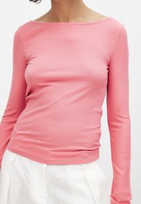 Rosa långärmad topp med ribbad textur och båtkrage, figurnära design. Matchad med ljusa, löst sittande byxor.