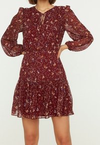 Vinsvart blommig klänning med långa genomskinliga ärmar, nyckelhålsringning, åtsittande midja och en utsvängd kjol med volangkant.