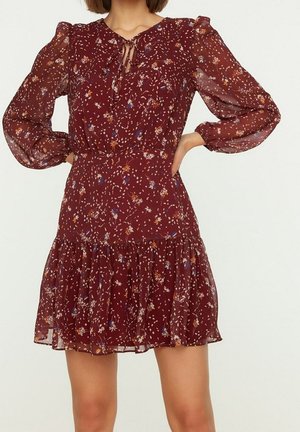 Vinsvart blommig klänning med långa genomskinliga ärmar, nyckelhålsringning, åtsittande midja och en utsvängd kjol med volangkant.