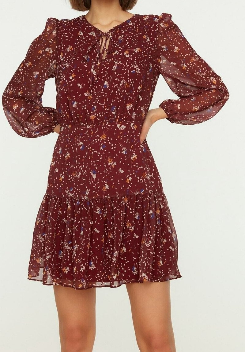 Vinsvart blommig klänning med långa genomskinliga ärmar, nyckelhålsringning, åtsittande midja och en utsvängd kjol med volangkant.