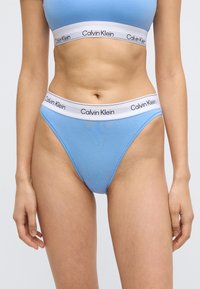 Μπλε thong από βαμβακερό μείγμα με λευκή ελαστική μέση που φέρει την επιγραφή "Calvin Klein" σε μαύρο. Λεπτή υφή, σχεδίαση χαμηλής μέσης.