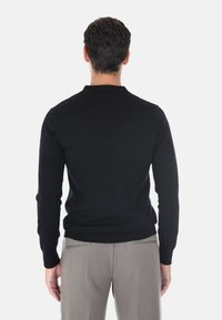 Maglione nero a maniche lunghe con colletto e orlo a coste, design aderente, mostrato da dietro, abbinato a pantaloni grigi chiari.