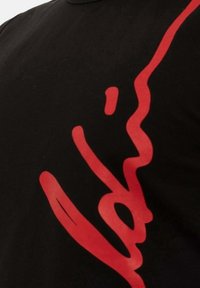 Schwarzes Baumwoll-T-Shirt mit einem auffälligen roten abstrakten Design, das die glatte Textur und die geschwungenen Linien auf der Stoffoberfläche betont.