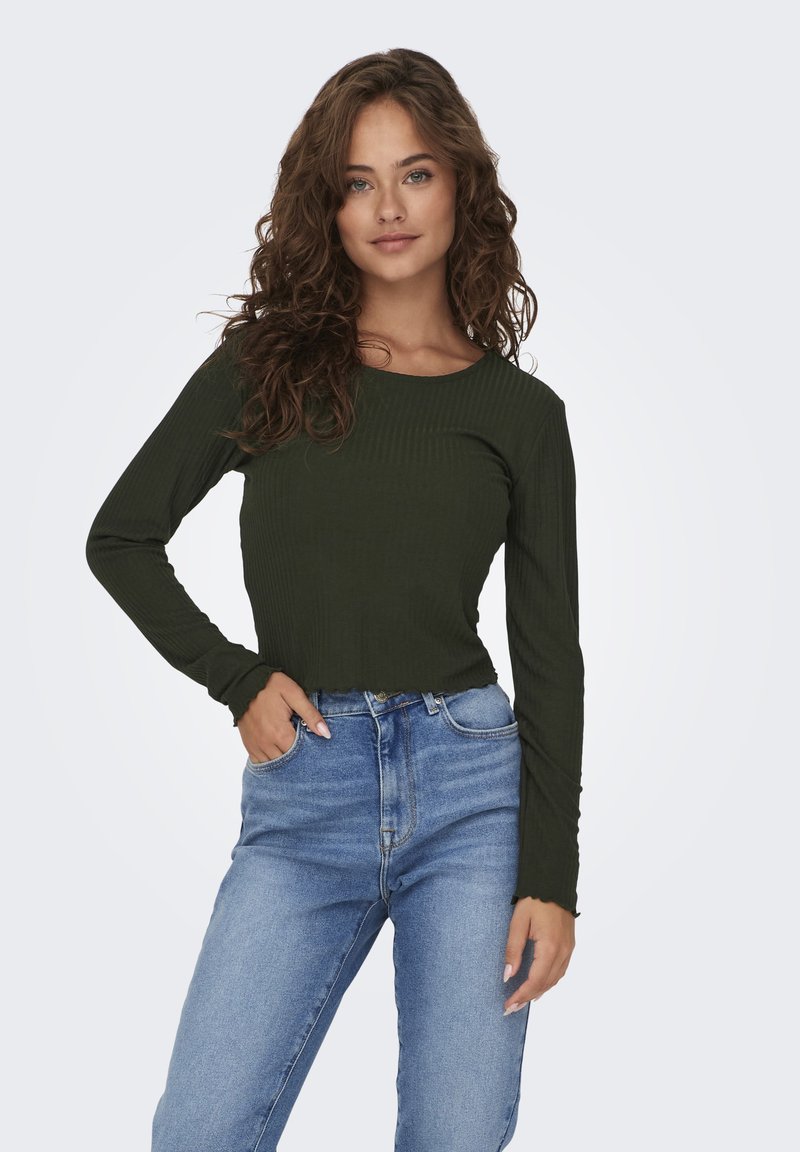 Långärmad, ribbad grön topp med rundad halsringning och vågig nederkant, som bärs med högmidjade, ljusblå jeans. Texturerat tyg synligt.