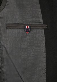 Innenseite der Jacke mit wiederholtem "HECHTER"-Textmuster, ausgestattet mit einer geknöpften Tasche mit einem schwarzen Knopf und einer rot-weiß-blauen Stoffschleife.