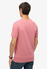 Kortärmad t-shirt med rund halsringning i blek rosa, med en strukturerad tygkvalitet och en avslappnad passform. Bakifrån visas en enkel design utan dekorationer.