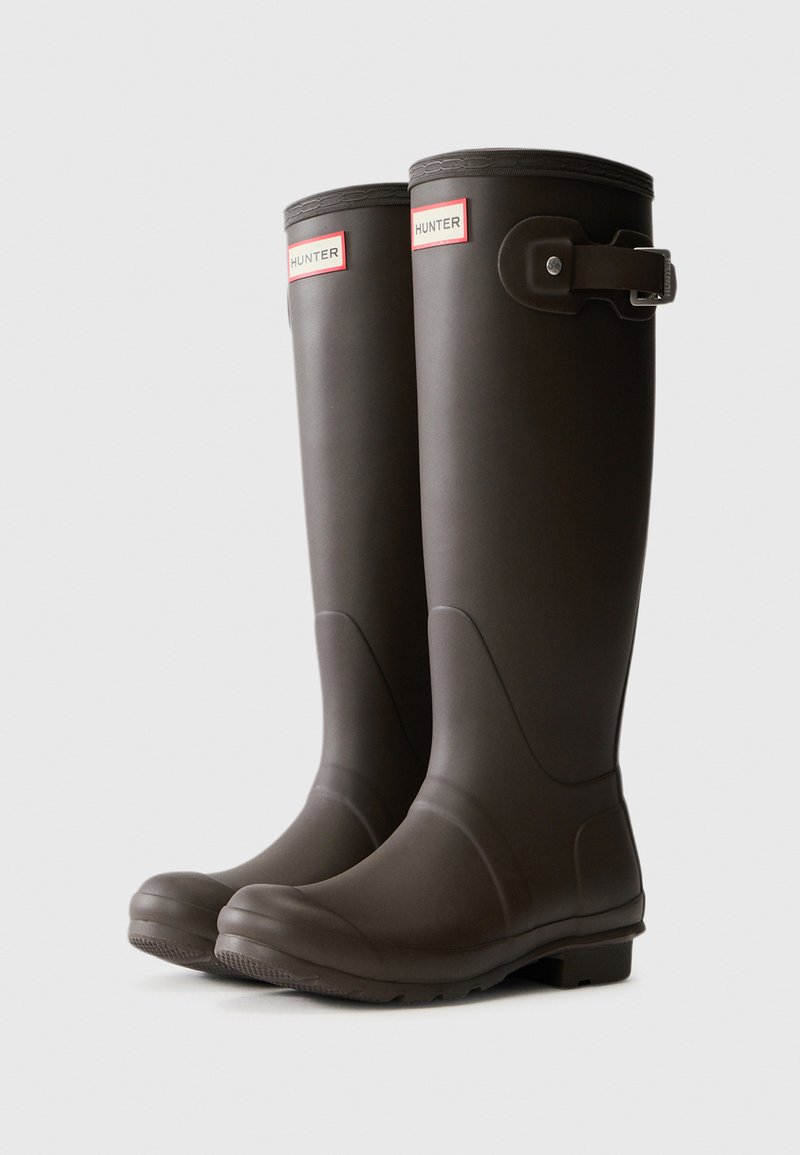 Braune Gummiregenstiefel mit abgerundeter Zehe, verstellbarem Schnallendetail und dem auffälligen "HUNTER"-Logo auf rotem Hintergrund nahe der oberen Kante.
