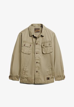 Beżowa kurtka robocza z zapięciem na guziki z przodu, dwoma kieszeniami na piersi i kieszeniami w szwach bocznych. Posiada wykładany kołnierz oraz metkę z logo.