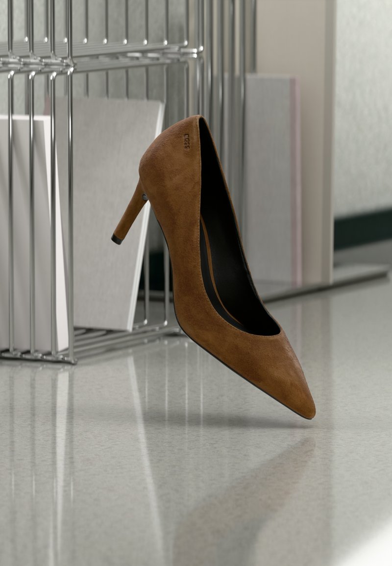 Chaussure à talon haut en daim marron équilibrée sur la pointe sur un sol poli à côté d'un organiseur de dossiers en métal avec des dossiers blancs.