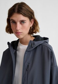 Mörkgrå huva jacka med en slät textur, som har en hel dragkedja, justerbar dragsko och ett svart fleecefoder på huvan.