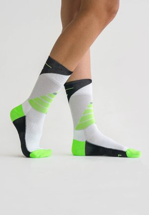 Weiße und schwarze Socken mit neongrünen Akzenten; sie verfügen über diagonale Muster, gerippte Texturen und ein eng anliegendes Knöcheldesign.