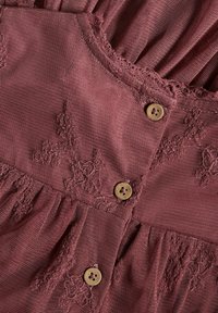 Bordeauxfarbenes Kleid mit zarter Spitzenverzierung, einem strukturierten Stoff und Holzknöpfen zum Verschließen. Enthält einen gerafften, fließenden Rock.