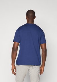 Navyblaue Baumwoll-T-Shirt mit rundem Halsausschnitt und kurzen Ärmeln, Ansicht von hinten, kombiniert mit hellgrauten Hosen. Glatte Textur, lässige Passform.
