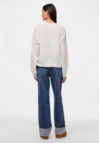 Oversized, light-colored sweater with dropped shoulders; paired with wide-leg blue jeans featuring a contrasting denim cuff at the hem.