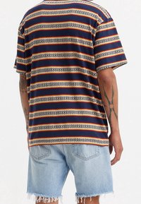 Gestreept T-shirt met korte mouwen in marineblauw, oranje en beige, met een geometrisch patroon. Draagt bijpassende vervaagde denimshorts met rafelige zoom.