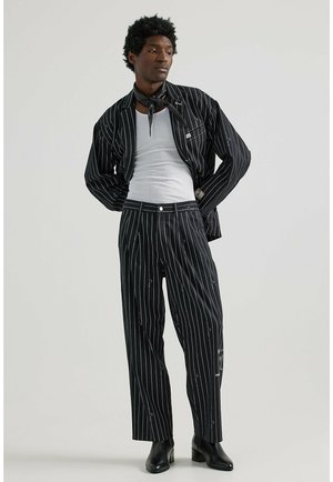 Schwarzes, gestreiftes Zweiteiler-Outfit aus strukturiertem Stoff, bestehend aus einer Knopfjacke und weiten Hosen, ergänzt mit einem schwarzen Schal.