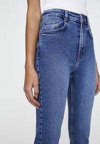 Jeans de denim azul de talle alto con un ajuste ceñido, que cuentan con bolsillos frontales, una cinturilla cosida y un ligero desgastado para añadir textura.