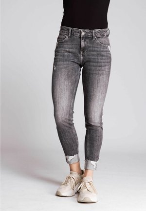 Hochwaisted, Skinny Jeans aus verblasstem schwarzem Denim mit distressed Details und rohem Saum. Kombiniert mit beigen Sneakern.