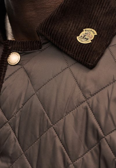 Καπιτονέ καφέ μπουφάν με γιακά από καμπαρντίνα, με κουμπιά με τα λογότυπα Barbour και Alexander Wang στο γιακά και στην περιοχή του στήθους.