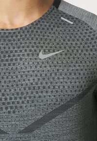 Detailaufnahme einer Person, die ein graues Nike Sportshirt mit Muster trägt, auf dessen Brust das Nike Swoosh-Logo zu sehen ist.