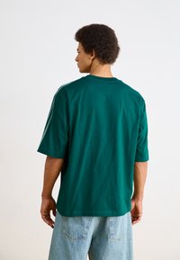 Grønne bomulds t-shirt med korte ærmer, rund hals og en afslappet pasform. Ingen synlige mønstre eller logoer, parret med lyseblå denim shorts.