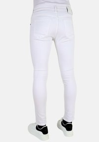 Witte skinny jeans van denim, met twee achterzakken en een platte tailleband, gecombineerd met zwart-witte sneakers.