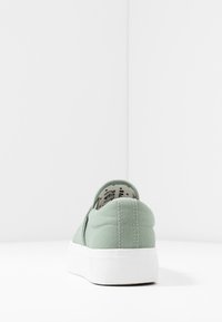 Baskets slip-on en toile de couleur vert doux, avec une texture et une semelle en caoutchouc blanc, des détails de couture simples et une doublure intérieure à motifs.