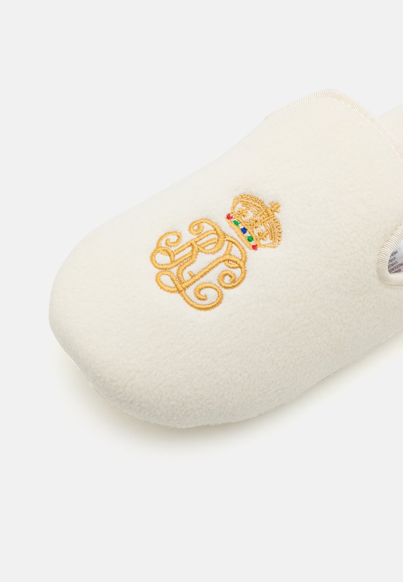 Chausson en polaire blanche avec un design de couronne brodée dorée et d'initiales. Forme arrondie, texture douce et bords surpiqués pour plus de durabilité.