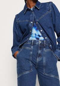 Denimskjorta med klassisk krage, knappstängning och puffärmar, ihop med högmidjade jeans med framträdande sömmar och fickor.