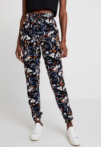Jogging neri con motivo floreale multicolore, vita elasticizzata con cordoncino e polsini aderenti. Indossati con sneakers bianche.