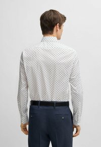 Witte langemouwige shirt met een marineblauw vierkant patroon, met een kraag en knoopsluiting aan de achterkant. Gecombineerd met donkere, gestructureerde broeken en een zwarte riem.
