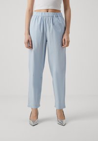 Lichtblauwe, losse broeken met een elastische tailleband, met een gladde textuur en taps toelopende pijpen. Gedragen met zilveren puntige hakken.