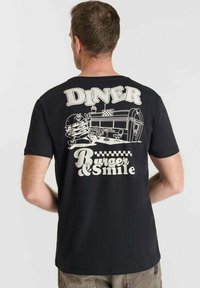 Camiseta de algodón negra con un gráfico de un diner retro en la parte posterior, con una ilustración de hamburguesa y un texto que dice "DINER Burger & Smile."